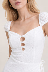 Robe en dentelle florale blanche de Dressie Dress, style romantique avec taille marquée et jupe wrap fendue, boutonnée sur le buste.