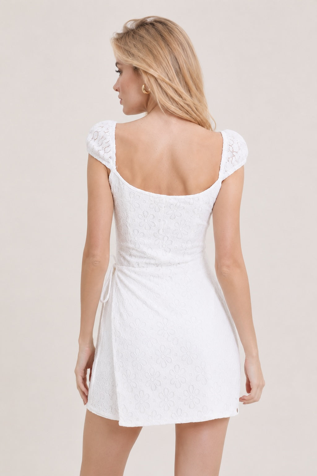 Robe en dentelle florale blanche de Dressie Dress avec taille marquée, jupe wrap fendue et détails boutonnés sur le buste.