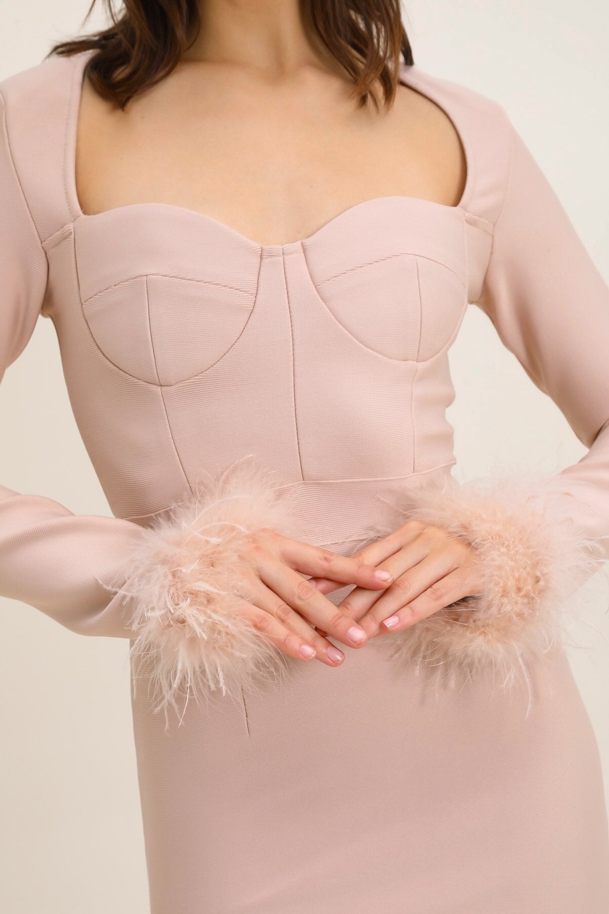 Robe bandage moulante beige à manches longues, décolleté en cœur et poignets ornés de plumes, élégante et sexy.