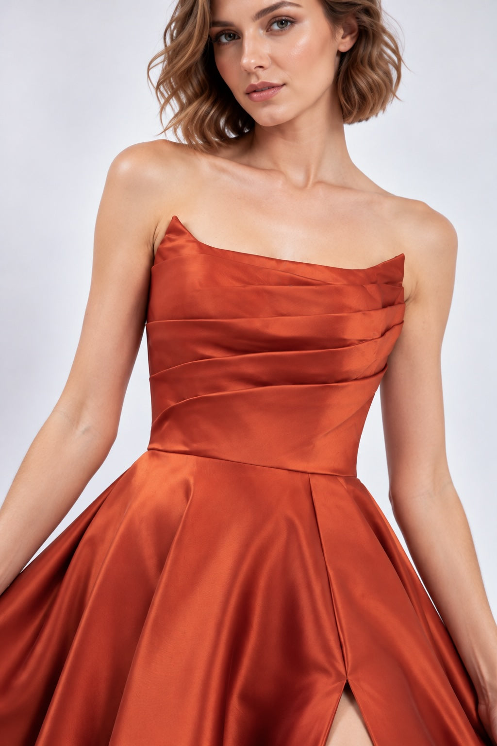 Robe de soirée bustier satinée brique avec drapé structuré, jupe volumineuse et fente élégante, robe chic pour fêtes et réveillon.
